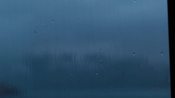 Eau de pluie forte chasse contre le verre de fenêtre bleu foncé et coulant vers le bas la nuit, fermer — Video