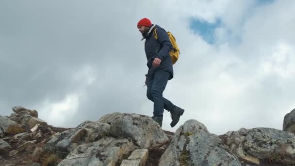 Man lopen op het hoogtepunt van een berg bij zonsondergang in slow motion, Noorwegen, Europa. Het dragen van een jas, Red Hat en gele rugzak — Stockvideo