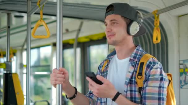 Young handsome men enjoying trip in the public transport, standing with headphone while moving in the modern tram — 비디오