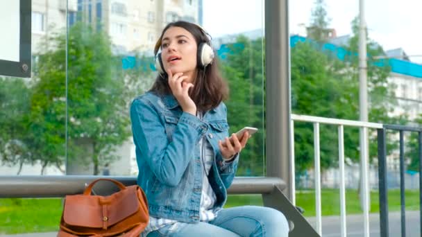 Девушка слушает музыку на современной автобусной остановке — стоковое видео