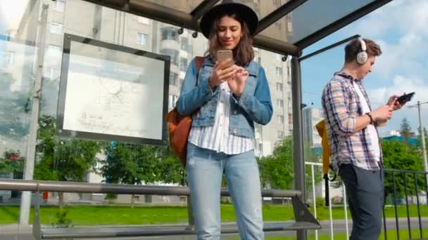 Zonnige dag, mensen staan bij de bushalte. met mobiele telefoons. Wachten op de bus. camera op steadicame — Stockvideo