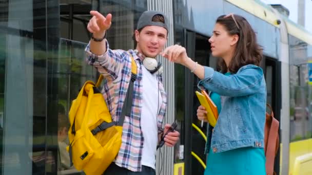 Vrolijke lachende man helpt verloren meisje toerist om weg te vinden. Verloren meisje toerist te vinden manier. Achtergrond tramstation. — Stockvideo