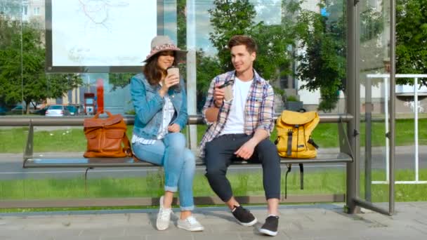 Fiatal pár kávézik a szabadban egy buszpályaudvari padon ülve — Stock videók