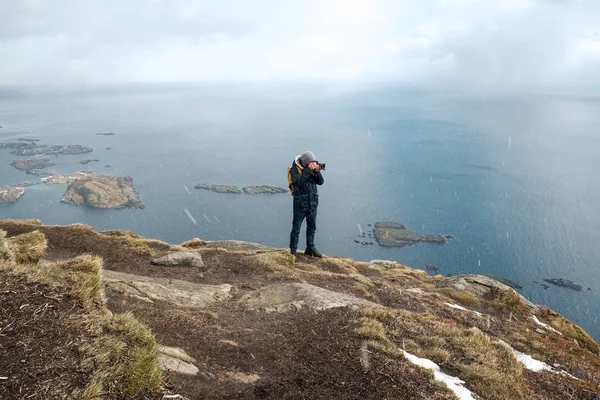 Jovem fotógrafo de pé na rocha nas montanhas na praia fotografando as paisagens nas ilhas Lofoten, na Noruega . — Fotografia de Stock