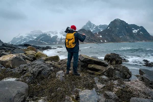 Joven fotógrafo de pie en la roca en las montañas en la playa fotografiando los paisajes en las Islas Lofoten en Noruega . — Foto de Stock