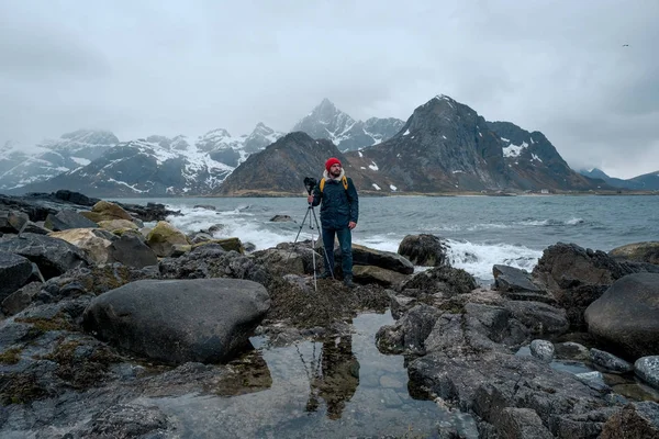 Nuori valokuvaaja seisoo kalliolla rannalla kuvaamassa maisemia Lofotensaarilla Norjassa . tekijänoikeusvapaita kuvapankkikuvia