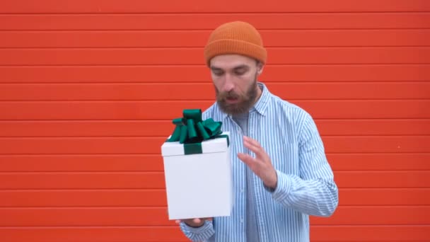 Bonito jovem hipster segurando caixa de presente em um fundo vermelho. Conceito de feriados e aniversários — Vídeo de Stock