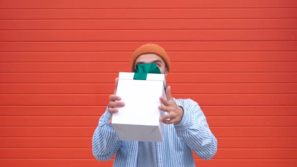 Веселый улыбающийся молодой человек ловит подарок на оранжевом фоне, замедленная съемка — стоковое видео