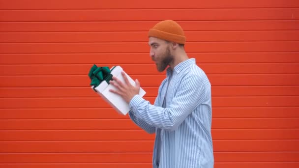 Jovem sorridente alegre pegando um presente no fundo laranja, câmera lenta — Vídeo de Stock