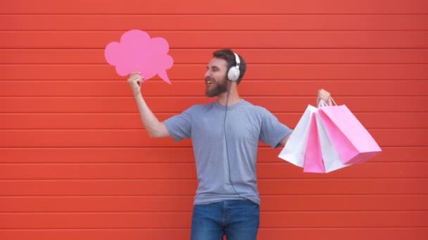 Surprised young man is holding a speech bubble, looking at camera and smiling, on red background — Stock Video