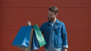 Mutlu modern adam alışveriş çantaları ve dişli bir gülümseme ile bir kredi kartı tutan, kameraya bakarak. kırmızı arka plan üzerinde