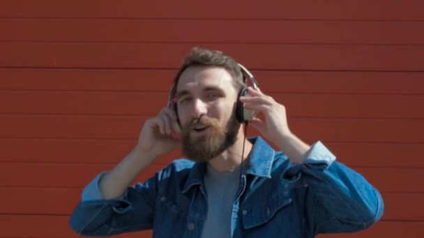 Jovem feliz com auscultadores. Ouvir música e dançar em um fundo vermelho. câmara lenta — Vídeo de Stock