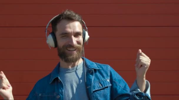 Joven feliz con auriculares. Escuchar música y bailar sobre un fondo rojo. cámara lenta — Vídeo de stock