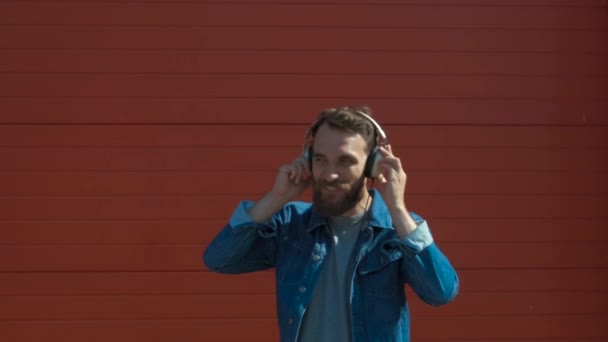 Gelukkige jonge man met koptelefoon. Luisteren naar muziek en dansen op een rode achtergrond. Slow Motion — Stockvideo