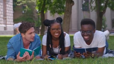 Okuma notları birlikte açık havada çim üzerinde oturan üç öğrencileri