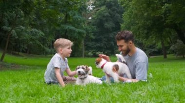 Küçük oğlu ile Sakal adam cynologist yeşil park yaz saatinde iki köpek ile yeşil bir çim üzerinde rahatlatıcı oynarken yalan. Aile, evcil hayvan, takım, dostluk evcil hayvan ve insan kavramı.