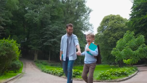 Eltern bringen ihr Kind zur Schule. Grundschüler gehen mit Rucksack ins Freie. Vater und Sohn gehen Hand in Hand. Unterrichtsbeginn. zurück zur Schule. erster Tag des Herbstes. Grundschüler. — Stockvideo