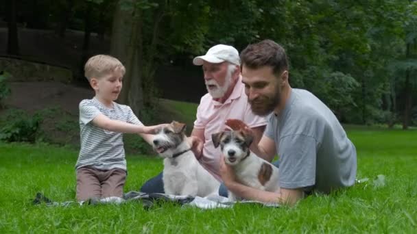 Familia multigeneracional paseando con perro. Papá abuelo e hijo con Jack Russel terrier divirtiéndose, riendo, besando, caminando juntos en el prado verde en el parque al aire libre . — Vídeo de stock