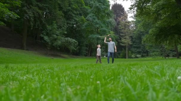 Papa et fils ensemble lancent l'avion modèle à l'extérieur, l'homme et le garçon regardent joyeusement l'avion. Père et fils passent du bon temps ensemble, concept de relations familiales. Pleine lumière . — Video