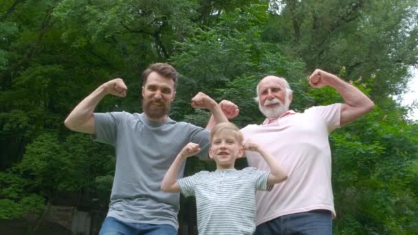 Retrato og família feliz avô, pai e seu filho sorrindo e mostrando seus músculos ao ar livre no parque no fundo. Três conceitos de geração diferentes . — Vídeo de Stock