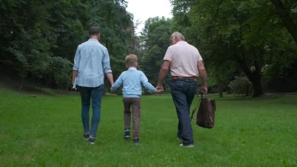 Famiglia Generazioni concetto: Padre, figlio e nonno, all'aperto, in natura, godendo il loro tempo di qualità insieme, Tutti in bella usura portare bambino a scuola. Vista posteriore . — Video Stock