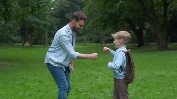 Imagen de un padre de barba moderno dando un hi-five a su pequeño hijo en el parque. Papá conoce a su hijo de la escuela primaria. el final del concepto de día escolar . — Vídeos de Stock