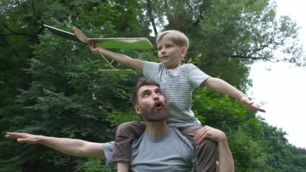 Батько віддає сина назад у парк. Батько і син будують разом паперовий літак. Портрет батька, який дає синові їзду на плечах. Подорожі відпочинок літо . — стокове відео
