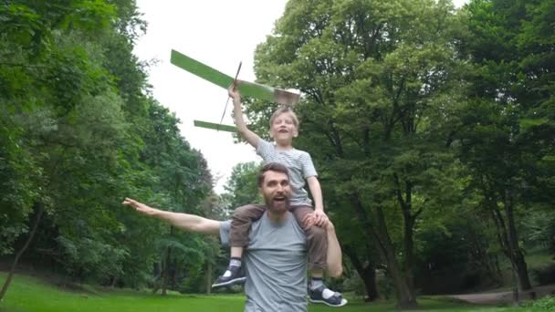 Papa et fils ensemble lancent l'avion modèle à l'extérieur, l'homme et le garçon regardent joyeusement l'avion. Père et fils passent du bon temps ensemble, concept de relations familiales. Pleine lumière . — Video