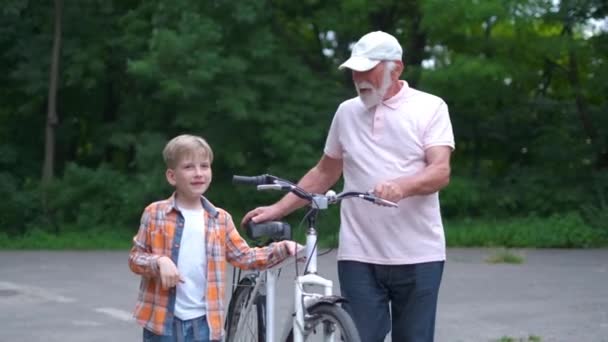 Feliz abuelo enseñando a niño a montar en bicicleta en el parque de verano. familia, generación, seguridad y concepto de personas — Vídeos de Stock