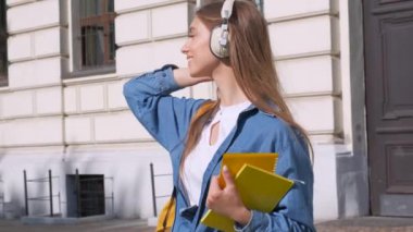 Mutlu sarışın kız gülümseyerek elinde bir dizüstü bilgisayar tutuyor ve kulaklık ile müzik dinliyor. okulun arka planına karşı görüntülemek. Üniversite öğrenimi kavramı