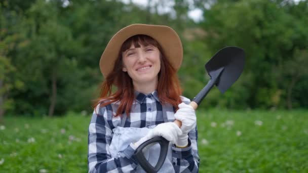 Jonge vrouw boer houden een schop en lachend in de tuin — Stockvideo