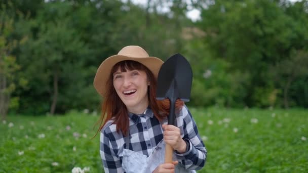 Молодая женщина фермер держит лопату и улыбается в саду — стоковое видео