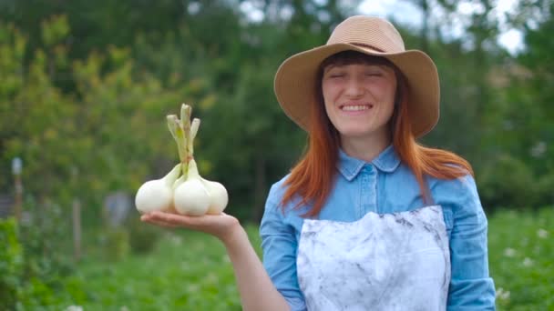 Portret vrouw houden van een bos van witte uien, staande in de buurt van de tuin — Stockvideo