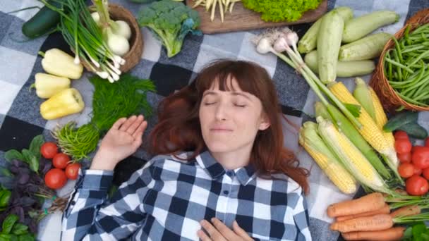 Retrato belo agricultor de mulher com olhos fechados que jaz em uma planície entre verduras orgânicas frescas. Vista superior. — Vídeo de Stock