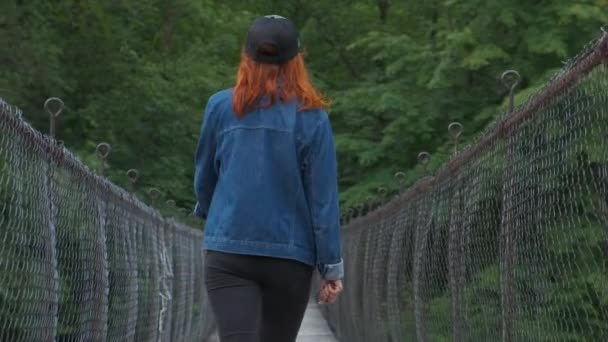 Jovem caminha na ponte suspensa — Vídeo de Stock