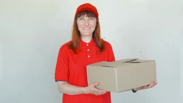 Dostawa uśmiechnięta kobieta w czerwonym mundurze. Samica w czapce, t-shirt, dżinsy pracujący jako Kurier lub sprzedawca posiadający pudełka tekturowe. — Wideo stockowe
