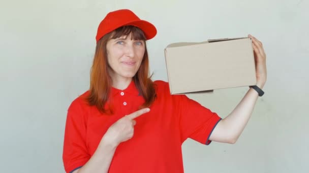 Entrega mulher sorridente em uniforme vermelho. Fêmea de boné, t-shirt, jeans trabalhando como estafeta ou comerciante segurando caixas de papelão . — Vídeo de Stock