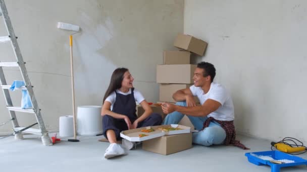 Vista aérea de la joven pareja comiendo pizza mientras está sentada en el piso en un apartamento nuevo — Vídeos de Stock