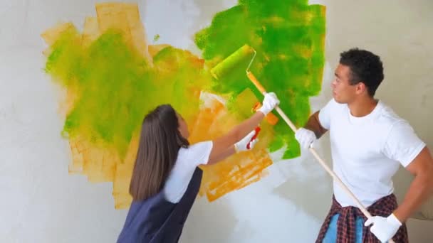 La giovane famiglia fa riparazioni nel nuovo appartamento. Coppia - parete di pittura in appartamento. Uomo e donna che stanno ristrutturando la casa. Divertente moglie e marito avendo buon umore fare decorare — Video Stock