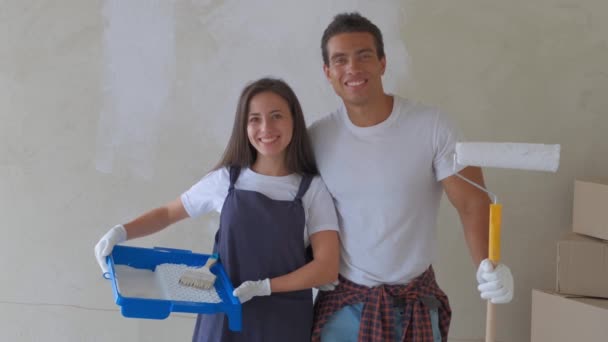 Retrato de um jovem casal em uma nova casa estão pintando e decorando a parede de sua casa — Vídeo de Stock