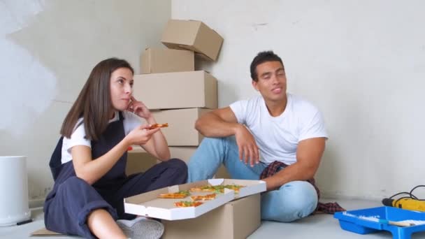 Happy young couple eating pizza during break in repairment — Stock Video