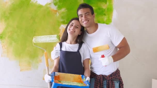 Casal rindo pintando sua casa verde posando juntos na frente de uma parede meio acabado com um rolo e banheira de tinta . — Vídeo de Stock