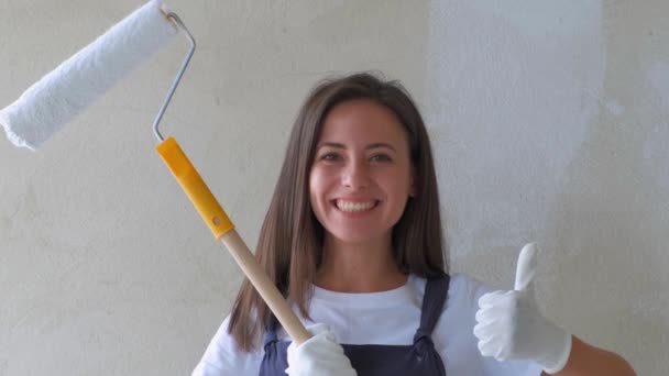 一个年轻女孩在修理。用滚筒的女孩粉刷墙壁。女孩做修理和微笑。粉刷房子里的墙壁。施工和维修。维修工作 — 图库视频影像