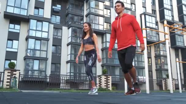 Image of young caucasian sporty man and woman 20s in tracksuits doing workout and squatting together in green park during sunny summer day. — Stock Video