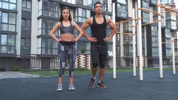 Sport par gör utfall på sommaren i staden, öva CrossFit. Sportkläder män och kvinnor i harmoni bakgrund stadsbyggnad. — Stockvideo