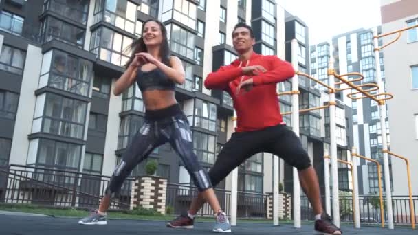 Fitness, sport, exercising and healthy lifestyle concept - man and woman doing squats outdoors in city — Stock Video