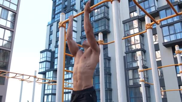 Hombre musculoso haciendo flexiones en la barra horizontal. en el área de entrenamiento cerca de la casa — Vídeo de stock