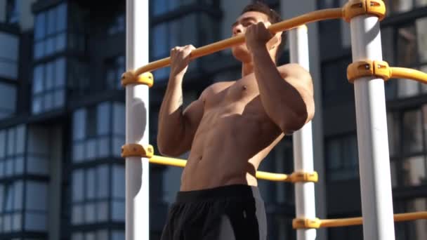 Мускулистый мужчина подтягивается на горизонтальной полосе. на тренировочной площадке рядом с домом — стоковое видео