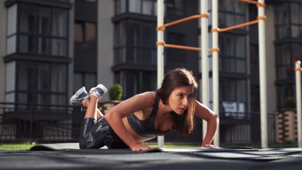 Fit κορίτσι κάνει pushup άσκηση υπαίθρια στην οδό της πόλης. γυμνασμένος γυναίκα που δουλεύει σε κοιλιακοί μύες και τρικέφαλες. Σπορ νεαρή γυναίκα κάνει push ups ασκήσεις. — Αρχείο Βίντεο