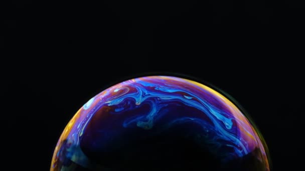 Colores multicolores del arco iris de una sola burbuja de jabón que parece un planeta de fantasía aislado sobre un fondo negro — Vídeo de stock